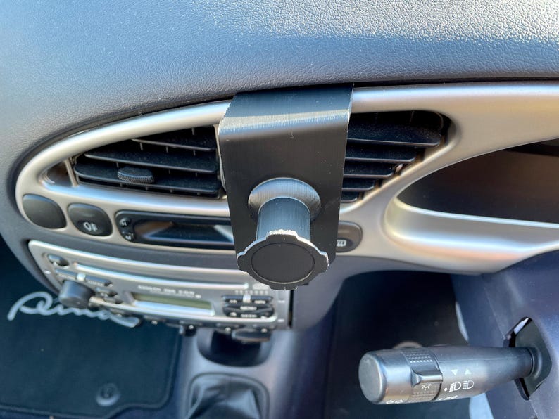 May include: A black car vent phone mount with a knob to adjust the angle. The mount is attached to a car's air vent.