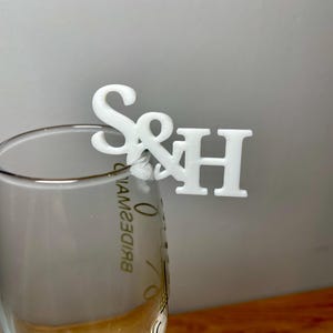 Champagne flute with a set of initial letters clipped onto the side. Drink topper is white and the photo shows a grey background.