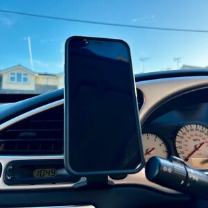 May include: A black smartphone is mounted in a car's dashboard using a phone holder. The phone's screen is black and the dashboard has a digital clock displaying 10:49.