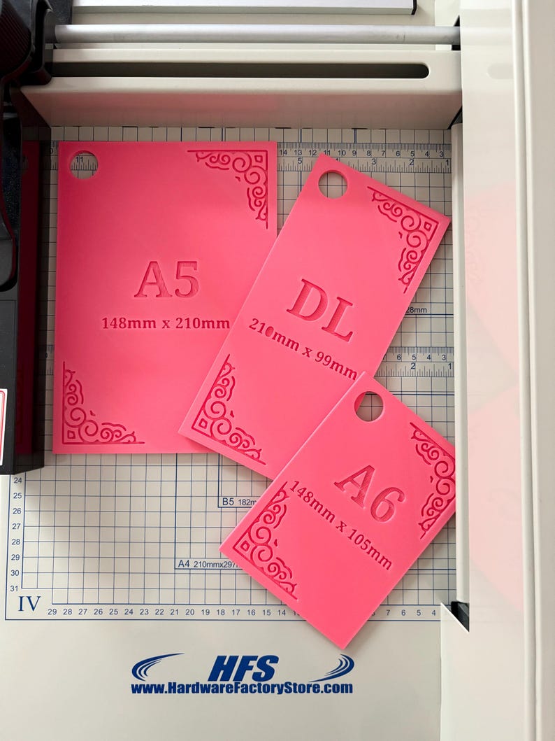 May include: Three bright pink rectangular templates with rounded corner cutouts and decorative scrollwork patterns. Each template is labeled with its size: A5 (148mm x 210mm), DL (210mm x 99mm), and A6 (148mm x 105mm), each featuring a circular hole for hanging.