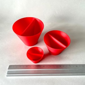 May include: Three red, cone-shaped objects with a central divider are displayed. A metal ruler with inch markings is placed next to the objects. The objects vary in size, with the largest approximately 4 inches in diameter.