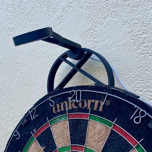 Dart board with attached lamp on the top. The lamp extends out in front of the board in order to cast light on the play area. Lamp is black modern design with a puck light at the end.