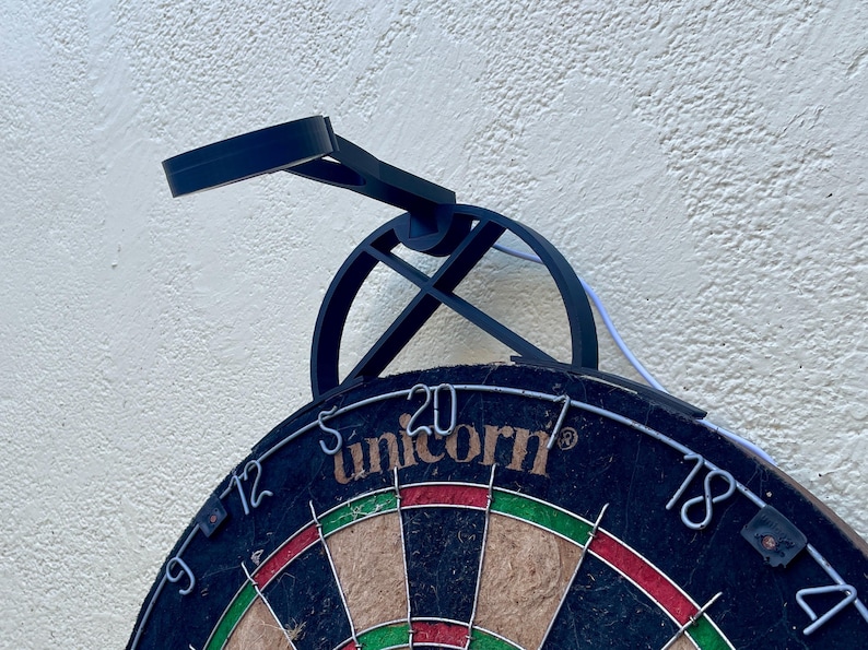 Dart board with attached lamp on the top. The lamp extends out in front of the board in order to cast light on the play area. Lamp is black modern design with a puck light at the end.