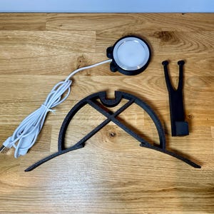 Dart board with attached lamp on the top. The lamp extends out in front of the board in order to cast light on the play area. Lamp is black modern design with a puck light at the end. Photo shows it deconstructed in 3 separate elements.