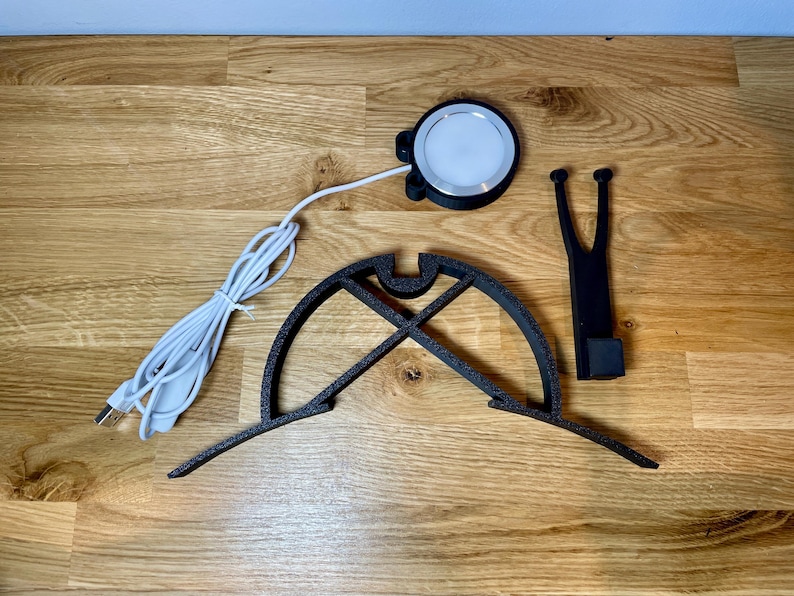 Dart board with attached lamp on the top. The lamp extends out in front of the board in order to cast light on the play area. Lamp is black modern design with a puck light at the end. Photo shows it deconstructed in 3 separate elements.
