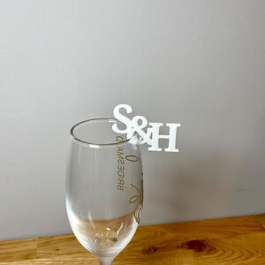 Champagne flute with a set of initial letters clipped onto the side. Drink topper is white and the photo shows a grey background.