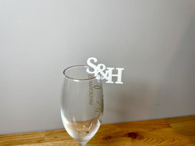 Champagne flute with a set of initial letters clipped onto the side. Drink topper is white and the photo shows a grey background.