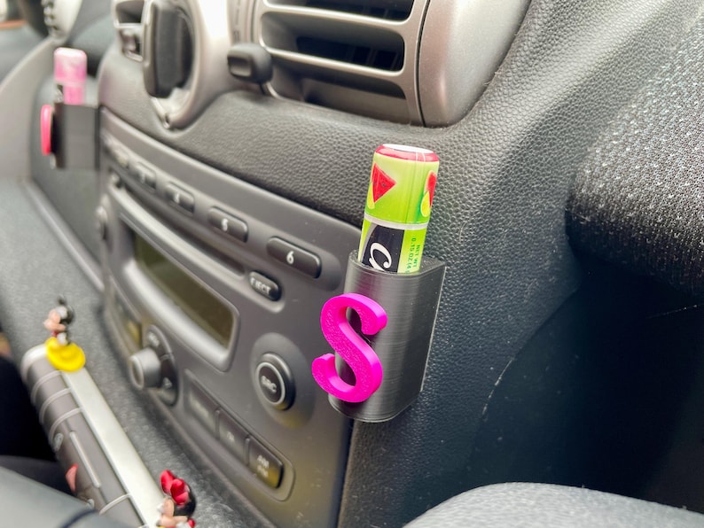 Pu&ograve; includere: Un porta cellulare per auto in plastica nera con una lettera "S" rosa stampata. Un tubo di balsamo per labbra verde e bianco &egrave; inserito nel supporto.