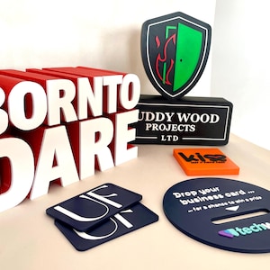 May include: A collection of promotional items, including a large red and white "BORN TO DARE" sign, a black shield-shaped logo with a green interior, and a dark blue oval with the text "techwyse".