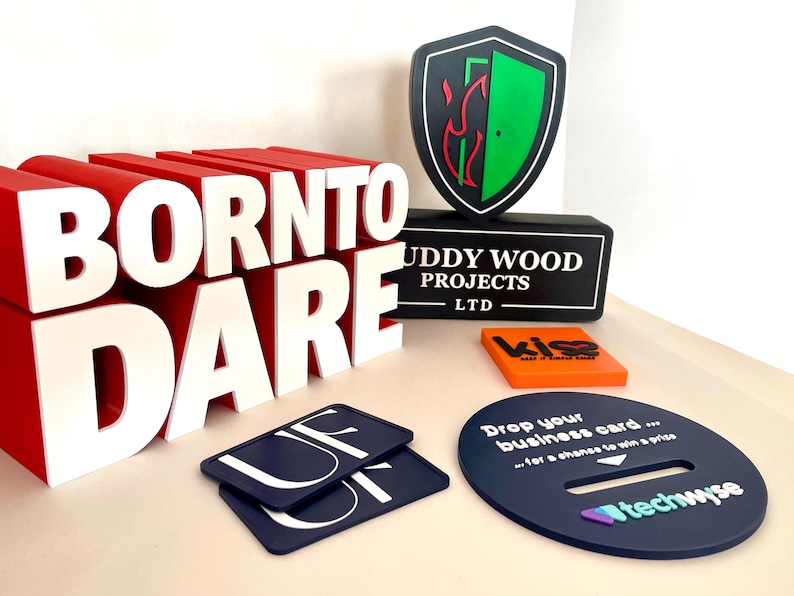 May include: A collection of promotional items, including a large red and white "BORN TO DARE" sign, a black shield-shaped logo with a green interior, and a dark blue oval with the text "techwyse".