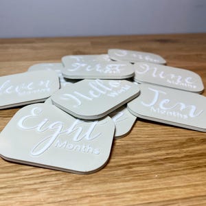 May include: A set of light green baby milestone cards with white lettering. The cards feature phrases like "Hello World", "Eight Months", and "Ten Months".