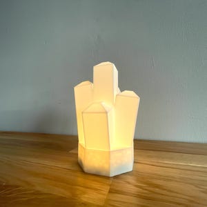 Pu&ograve; includere: Una lampada in ceramica bianca a forma di grappolo di cristalli. La lampada &egrave; accesa ed emette una luce calda.