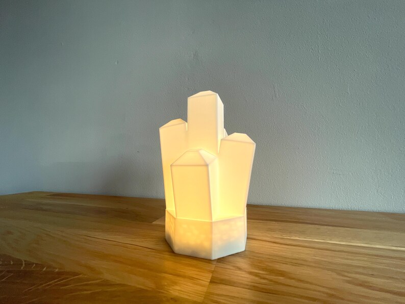 Pu&ograve; includere: Una lampada in ceramica bianca a forma di grappolo di cristalli. La lampada &egrave; accesa ed emette una luce calda.