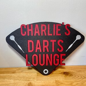 Triangular darts sign with the text charlie's darts lounge in red. Main background is black and has silver inlayed darts logos.