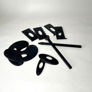 May include: A collection of black pottery tools, including various shaped scrapers, oval-shaped tools, and two long, thin tools. The tools are arranged on a white surface, providing a clear view of their shapes and designs.