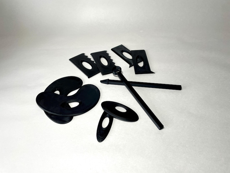 May include: A collection of black pottery tools, including various shaped scrapers, oval-shaped tools, and two long, thin tools. The tools are arranged on a white surface, providing a clear view of their shapes and designs.