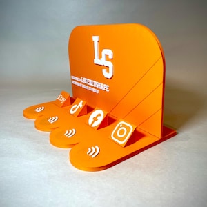 May include: An orange acrylic display stand with white text and social media icons. The stand features the Etsy, TikTok, Facebook, and Instagram logos. The text on the stand reads "LS" and "LAYEREDSHAPE".