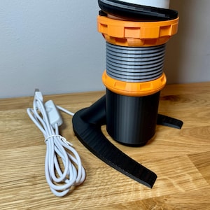 Op de afbeelding: Een zwart-oranje 3D-geprinte lamp met een spiraalvormig ontwerp en een wit snoer met een schakelaar.