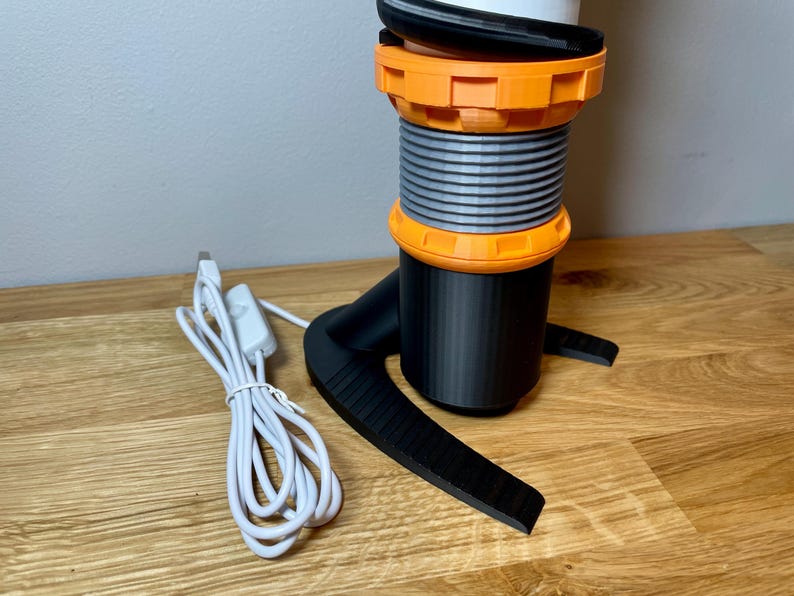 Op de afbeelding: Een zwart-oranje 3D-geprinte lamp met een spiraalvormig ontwerp en een wit snoer met een schakelaar.