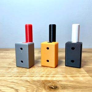 Op de afbeelding: Drie kleine, rechthoekige dozen met verschillende gekleurde bovenkanten. De doos links heeft een rode bovenkant, de middelste doos heeft een oranje bovenkant en de doos rechts heeft een zwarte bovenkant.