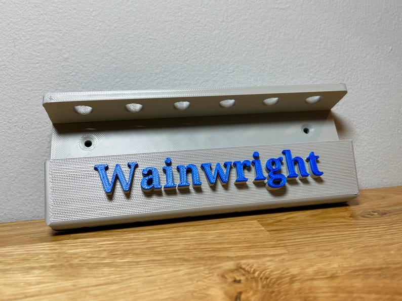 Wall mounted dart holder. Silver with Blue personalised text on the front reading Wainwright