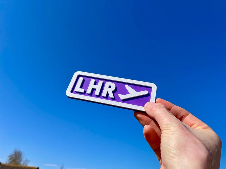 May include: Purple sign with white lettering that reads "LHR" and a white airplane icon pointing to the right.