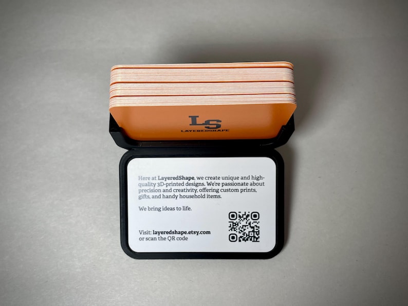 May include: A black case holds a stack of orange and white cards. The top card has the text "LS LAYEREDSHAPE". The case also displays text: "Here at LayeredShape...We bring ideas to life." and a QR code. Visit layeredshape.etsy.com.