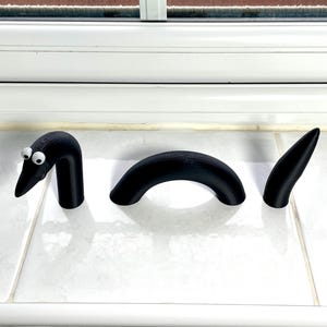 May include: Three black 3D printed worm segments, one with googly eyes, on a white tiled surface.