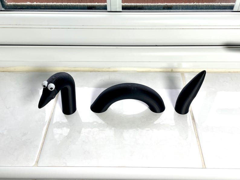 May include: Three black 3D printed worm segments, one with googly eyes, on a white tiled surface.