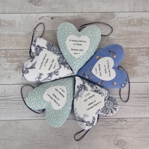 May include: Five heart-shaped fabric cushions with floral patterns and embroidered messages. The messages say "In loving memory of Hazel, Always with you x".