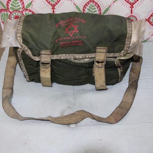 May include: A green canvas messenger bag with a tan strap and a red Star of David logo. The logo reads "צה"ל" in Hebrew, which translates to "IDF" (Israel Defence Forces).