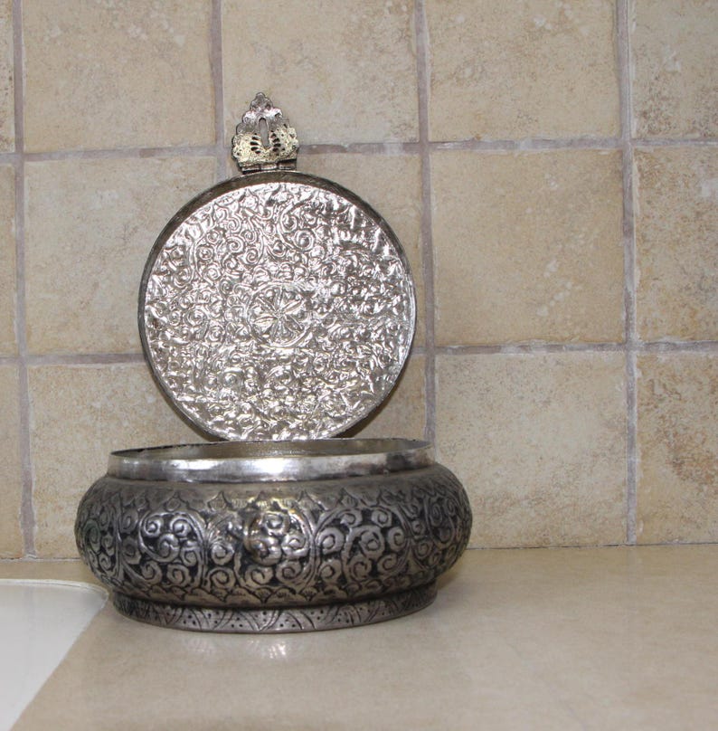 May include: A silver trinket box with an ornate floral design. The lid is open and has a small decorative knob on top.