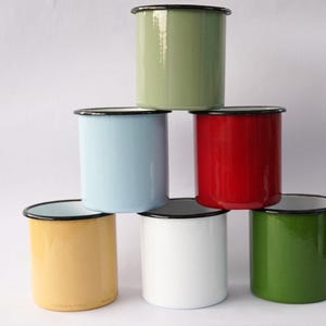 Puede incluir: Seis tazas de esmalte en diferentes colores: verde, azul claro, rojo, amarillo, blanco y verde oscuro. Las tazas están apiladas en forma de pirámide.