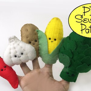 May include: A set of five felt finger puppets shaped like vegetables: a red chilli pepper, a white garlic clove, a brown potato, a yellow corn cob, and a green artichoke. Each puppet has a smiling face with black eyes and a stitched-on mouth. The puppets are arranged on a hand, with the chilli pepper on the pinky finger and the artichoke on the thumb. The text "PDF Sewing Pattern" is written in black on a yellow oval in the top right corner of the image.