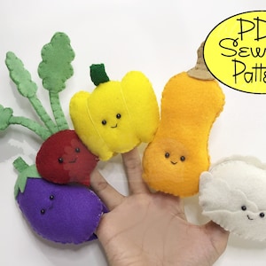 May include: Five felt finger puppets shaped like vegetables: a purple eggplant, a red radish with green leaves, a yellow bell pepper, an orange butternut squash, and a white dumpling. The puppets have smiling faces and are arranged on a hand.
