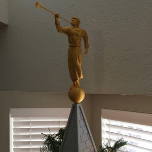 May include: A gold angel figurine playing a trumpet on top of a gray pyramid-shaped Christmas tree topper.