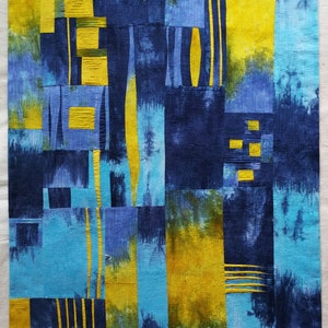 Può includere: Trapunta d'arte astratta con un design a patchwork composto da quadrati di tessuto blu, giallo e verde. La trapunta è composta da varie forme e motivi geometrici.