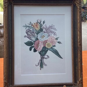 Puede incluir: Una impresión enmarcada de un ramo de flores coloridas, incluyendo rosas rosas, tulipanes morados y flores blancas. La impresión está enmarcada en un marco de madera oscuro y ornamentado, sobre un caballete de madera. Estilo vintage.