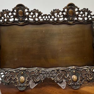 Puede incluir: Una bandeja de servir antigua de color bronce con detalles de filigrana ornamentados. La bandeja presenta un centro rectangular con asas decorativas y un borde detallado. El diseño incluye acentos ovalados y patrones de volutas.