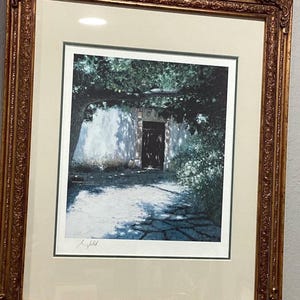Puede incluir: Una impresión enmarcada de una pintura que representa una puerta con un arco de piedra y una puerta de madera. La puerta está rodeada de vegetación exuberante y la escena está bañada por una luz suave.