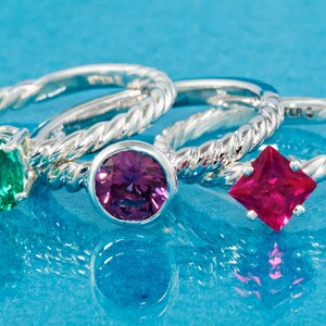 K&ouml;nnte beinhalten: Drei Silberringe mit verschiedenen Edelsteinen. Der Ring links hat einen gr&uuml;nen Smaragd, der mittlere Ring einen violetten Amethyst und der Ring rechts einen roten Rubin.