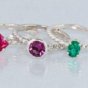 K&ouml;nnte beinhalten: Drei Silberringe mit verschiedenen Edelsteinen. Der Ring links hat einen quadratischen roten Edelstein, der mittlere Ring einen runden violetten Edelstein und der Ring rechts einen ovalen gr&uuml;nen Edelstein.