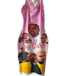 May include: A sleeveless pink dress featuring multiple images of Chris Brown. The dress has a bodycon silhouette and the words "Chris Brown" are printed in a cursive font across the front.