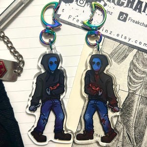 May include: Two clear acrylic keychains featuring a character in a black hoodie, blue mask, and blue jeans. One keychain shows the character holding a red heart, the other holding a red heart and a knife. Both have iridescent crescent moon clasps.