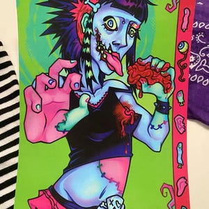 May include: A rectangular art print featuring a blue-skinned zombie character with spiky black hair, wearing a black top and pink skirt. The character has stitches on their skin, a long tongue, and holds a red mass. A pink border displays small icons.