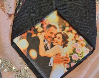 Puede incluir: Corbata negra con un patrón texturizado, que presenta una imagen impresa de una pareja abrazándose. La imagen es un primer plano de un hombre y una mujer, probablemente una foto de boda, con un fondo floral.