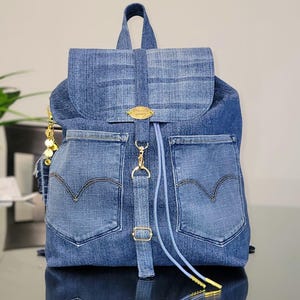 May include: A denim backpack with a flap closure and two front pockets. The backpack features gold-colored hardware, including a clasp and decorative accents. The design incorporates the classic Levi's pocket shape and stitching.