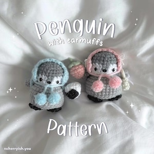 May include: Two crocheted penguin amigurumi toys wearing earmuffs. One penguin is gray with blue earmuffs and the other is gray with pink earmuffs. The penguins are holding a strawberry and a black and white ball. The text "Penguin with earmuffs Pattern" is below the penguins.