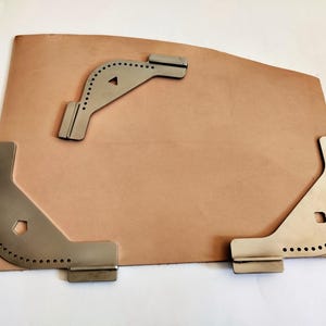 Peut inclure: Une peau de cuir marron clair avec trois outils d'angle en m&eacute;tal argent&eacute;. Les outils pr&eacute;sentent de petits trous le long des bords incurv&eacute;s. Un outil est triangulaire, les autres sont en forme de L.