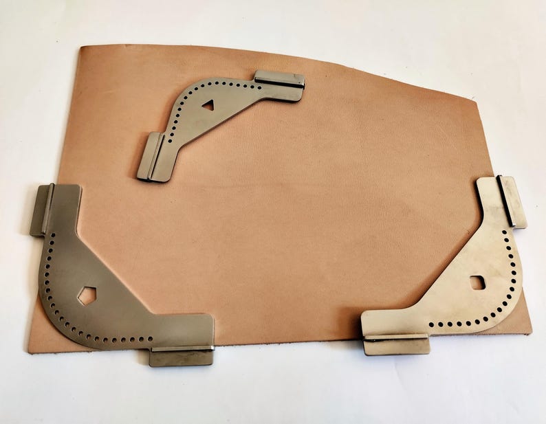 Peut inclure: Une peau de cuir marron clair avec trois outils d'angle en m&eacute;tal argent&eacute;. Les outils pr&eacute;sentent de petits trous le long des bords incurv&eacute;s. Un outil est triangulaire, les autres sont en forme de L.